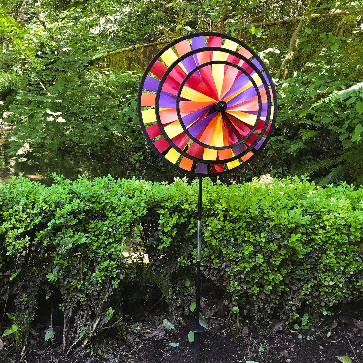 Vibrant Autumn Triple Wheel Spinner featuring three colorful wheels dancing in the wind, showcasing fall hues of red, orange, and yellow in a garden setting.