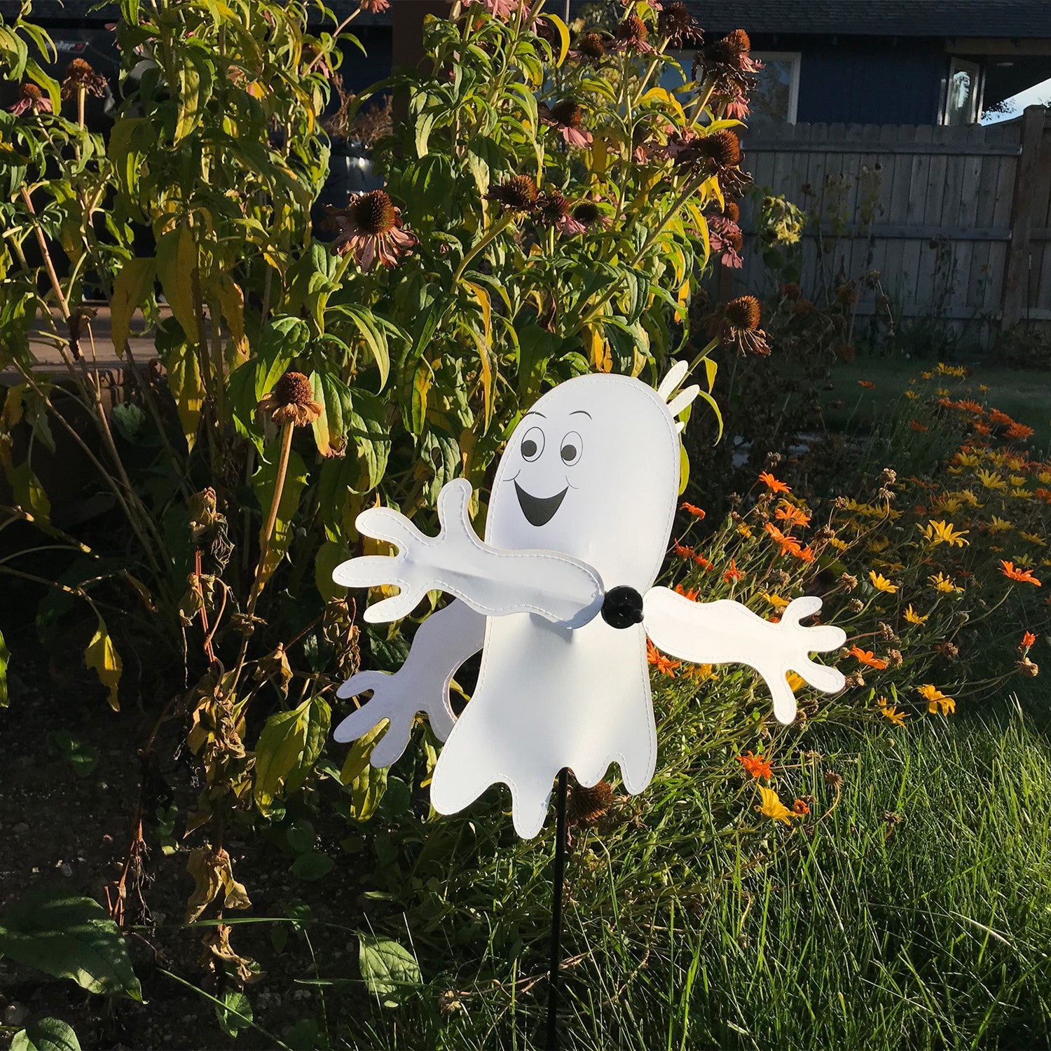 Baby Ghost Whirligig spinning in outdoor garden setting, featuring a cheerful ghost design perfect for Halloween decor.