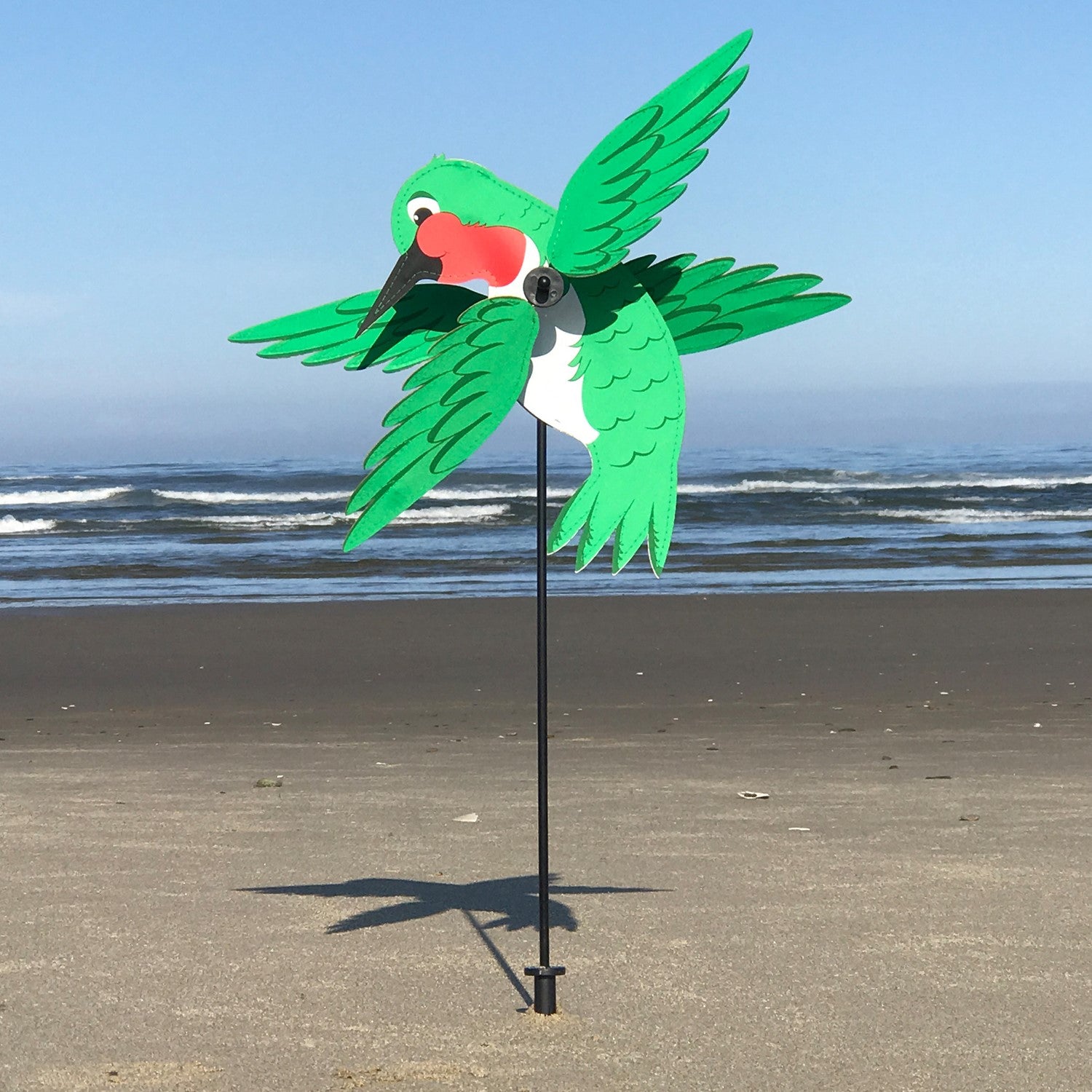 Baby Hummingbird Whirligig in bright colors spins in a garden setting, showcasing its whimsical design and durable construction.