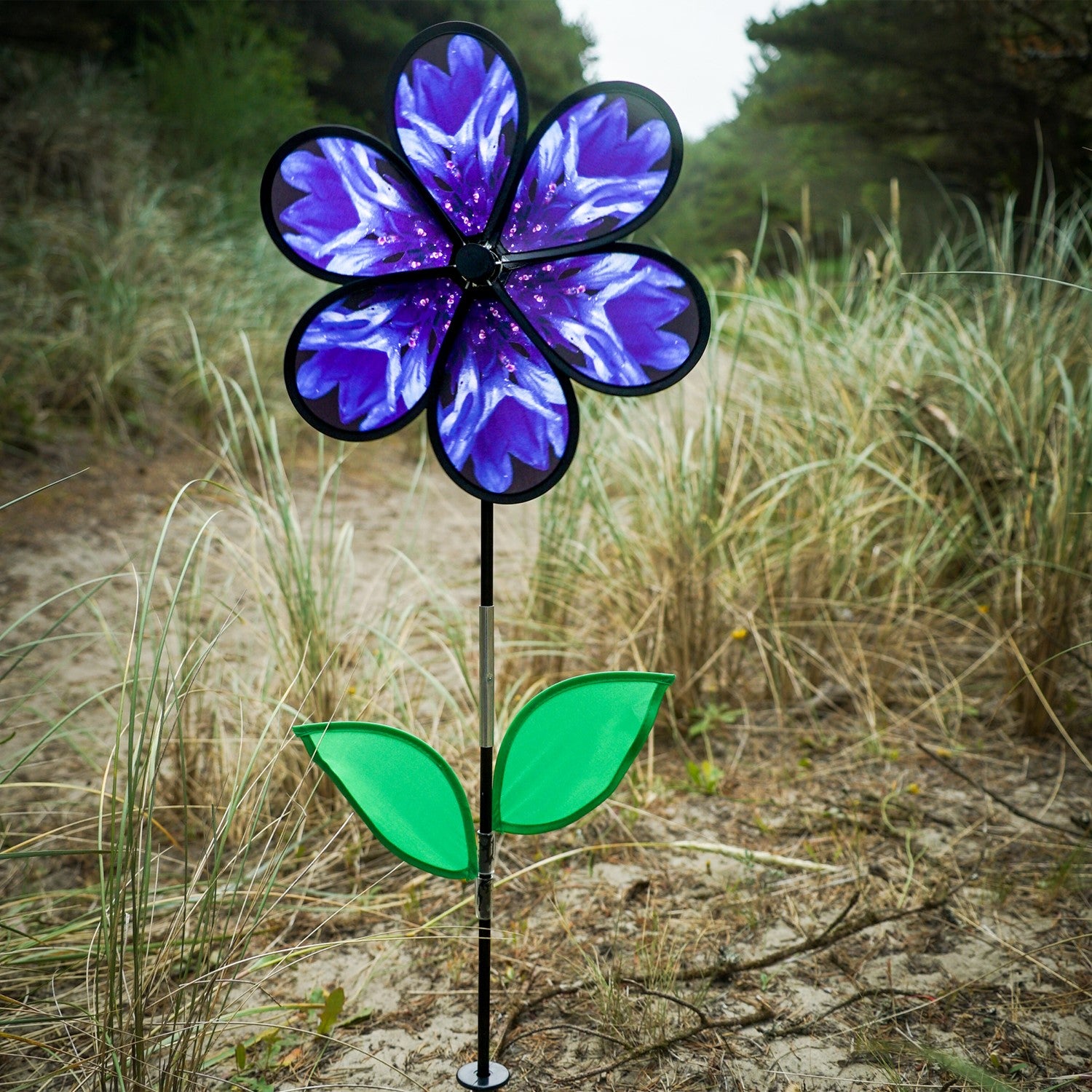 Vibrant 13.5-inch Bachelor Button Spinner with realistic blue flower and green leaves spinning on a fiberglass pole in a garden setting.