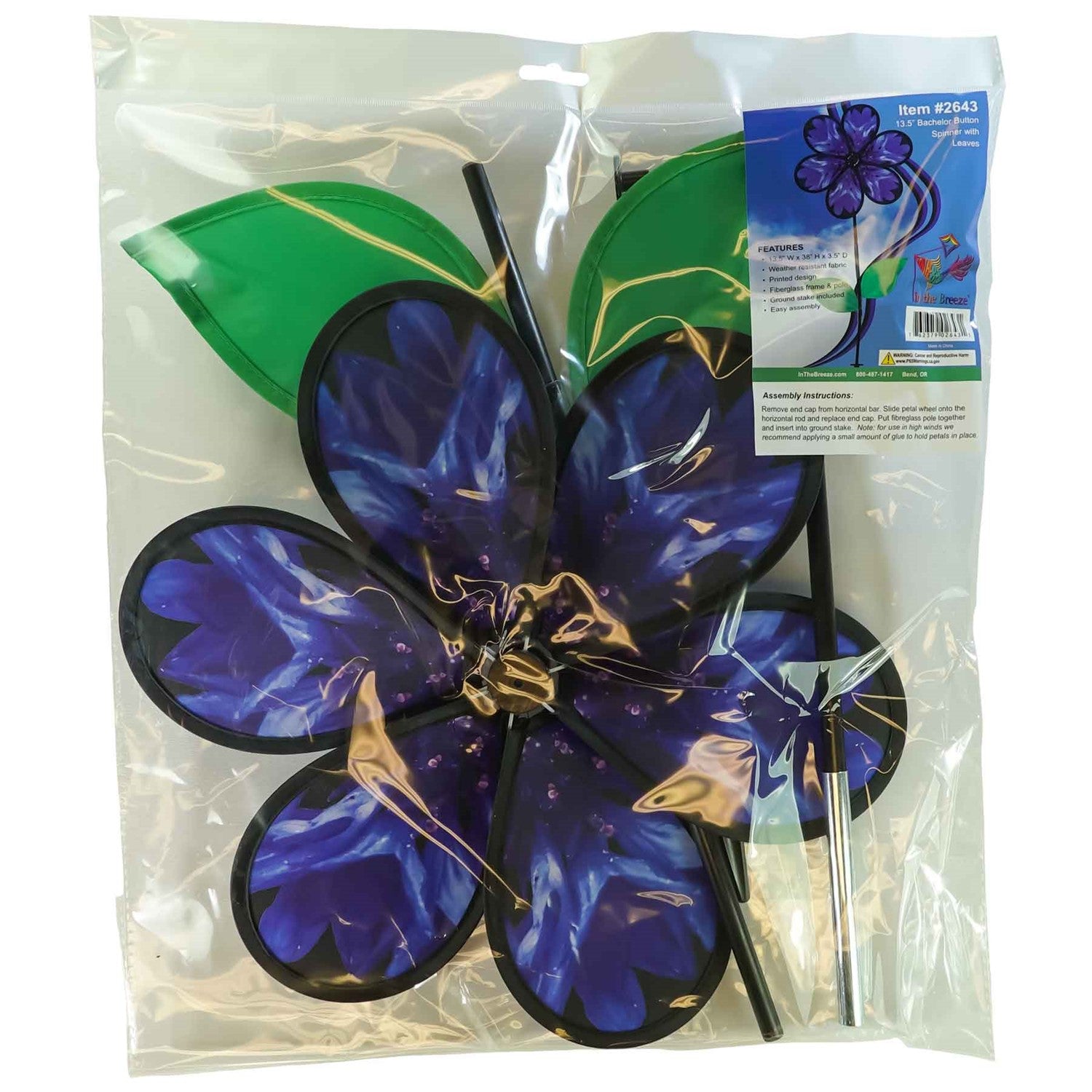 Vibrant 13.5-inch Bachelor Button Spinner with realistic blue flower and green leaves spinning on a fiberglass pole in a garden setting.