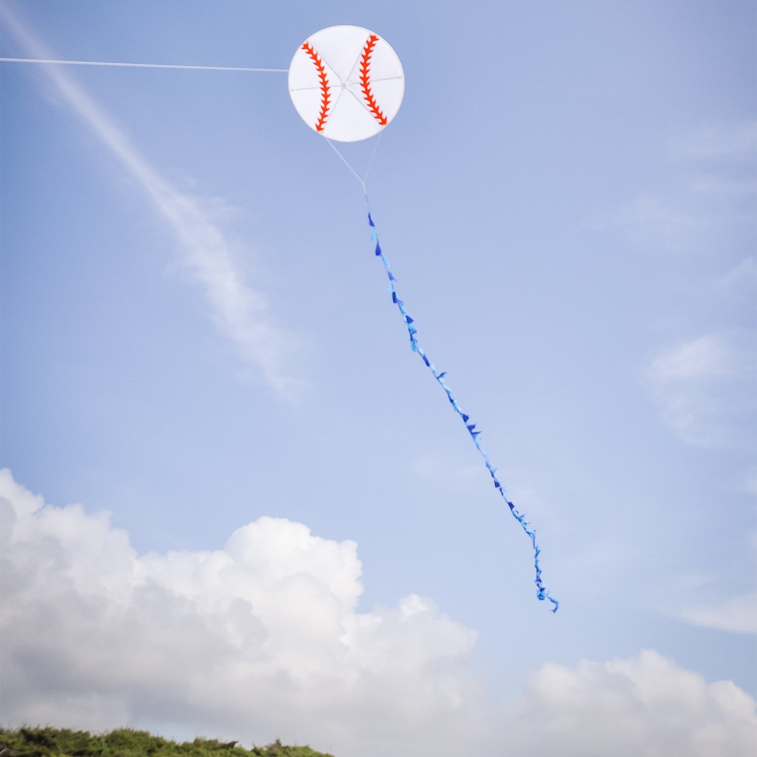 Baseball Kite featuring red stitching on a white background with a long blue triangle tail flying high against a blue sky.