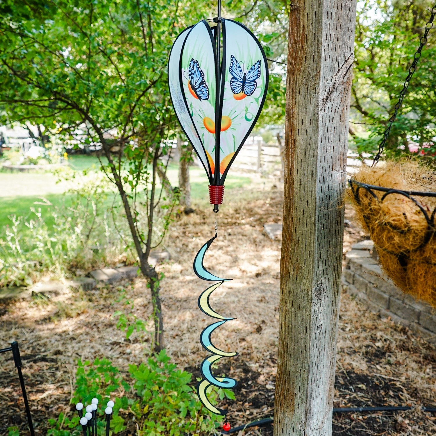 Colorful Blue Butterfly Hot Air Balloon spinner with butterfly design and daisies, displayed outdoors, showcasing movement in a garden setting.