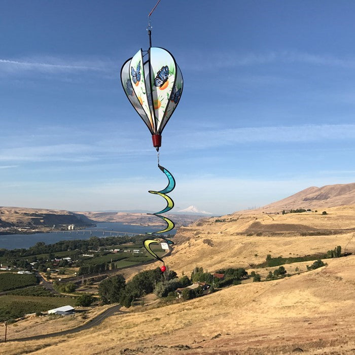 Colorful Blue Butterfly Hot Air Balloon spinner with butterfly design and daisies, displayed outdoors, showcasing movement in a garden setting.