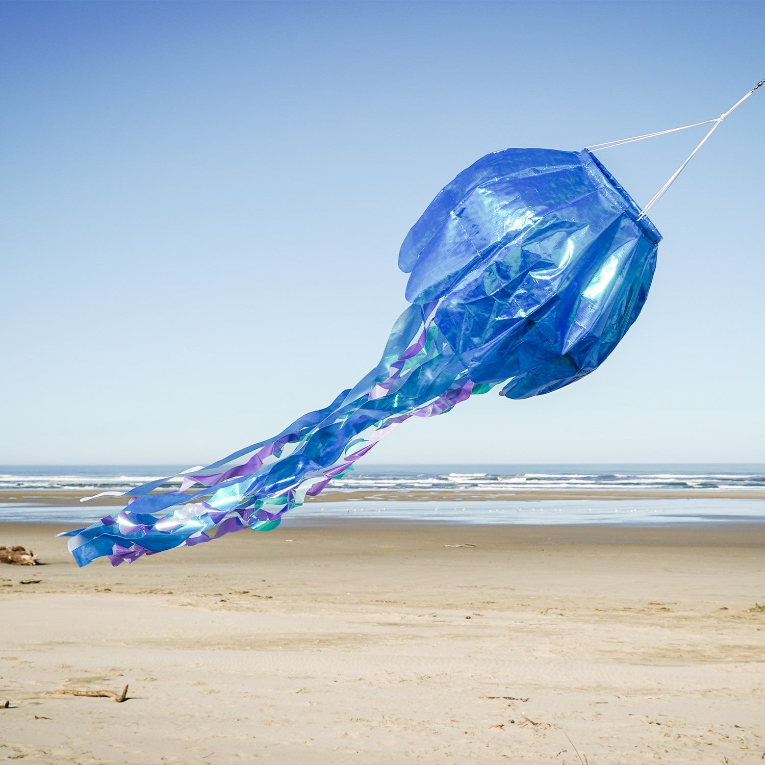 50-inch blue iridescent jellyfish 3D windsock with flowing tentacles, showcasing vibrant colors against a garden backdrop, fluttering in the wind.