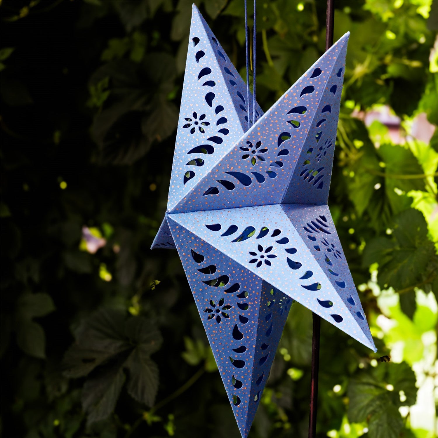 Blue Paper Star Lantern with intricate cutouts, hung indoors, providing a glowing ambiance in a boho-inspired setting.