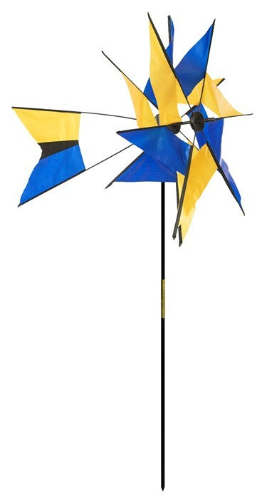Blue and Yellow Kaleidoscope Ground Spinner displaying vibrant colors on a pivoting sail, gracefully rotating in an outdoor garden setting.