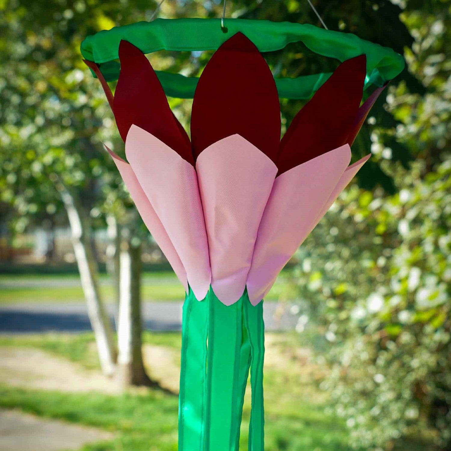 Burgundy 38' Lotus Flower Windsock with colorful petals and flowing green tails swaying gently in the breeze, enhancing a garden space.