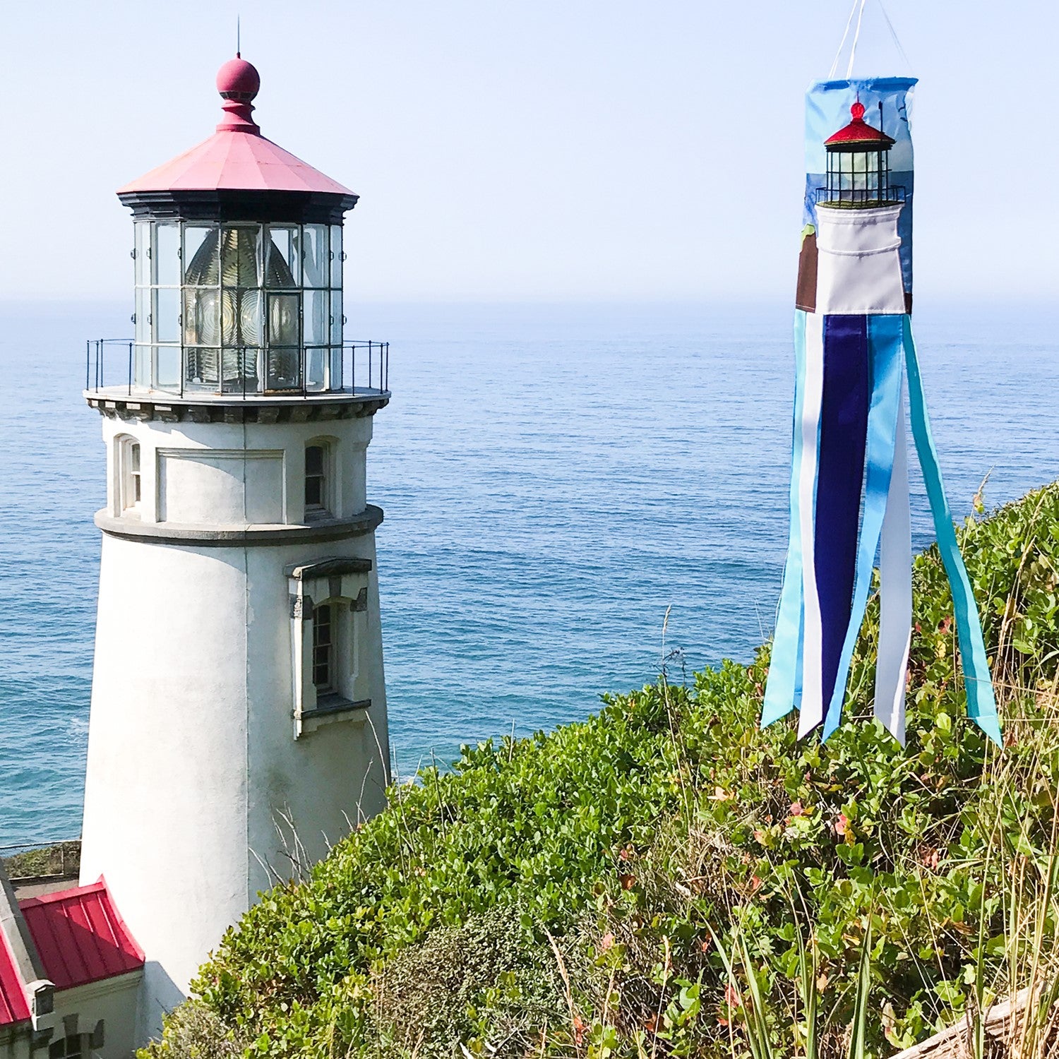 Coastal Lighthouse 40-inch windsock with vibrant lighthouse design and tails hanging elegantly from a garden in a coastal setting.