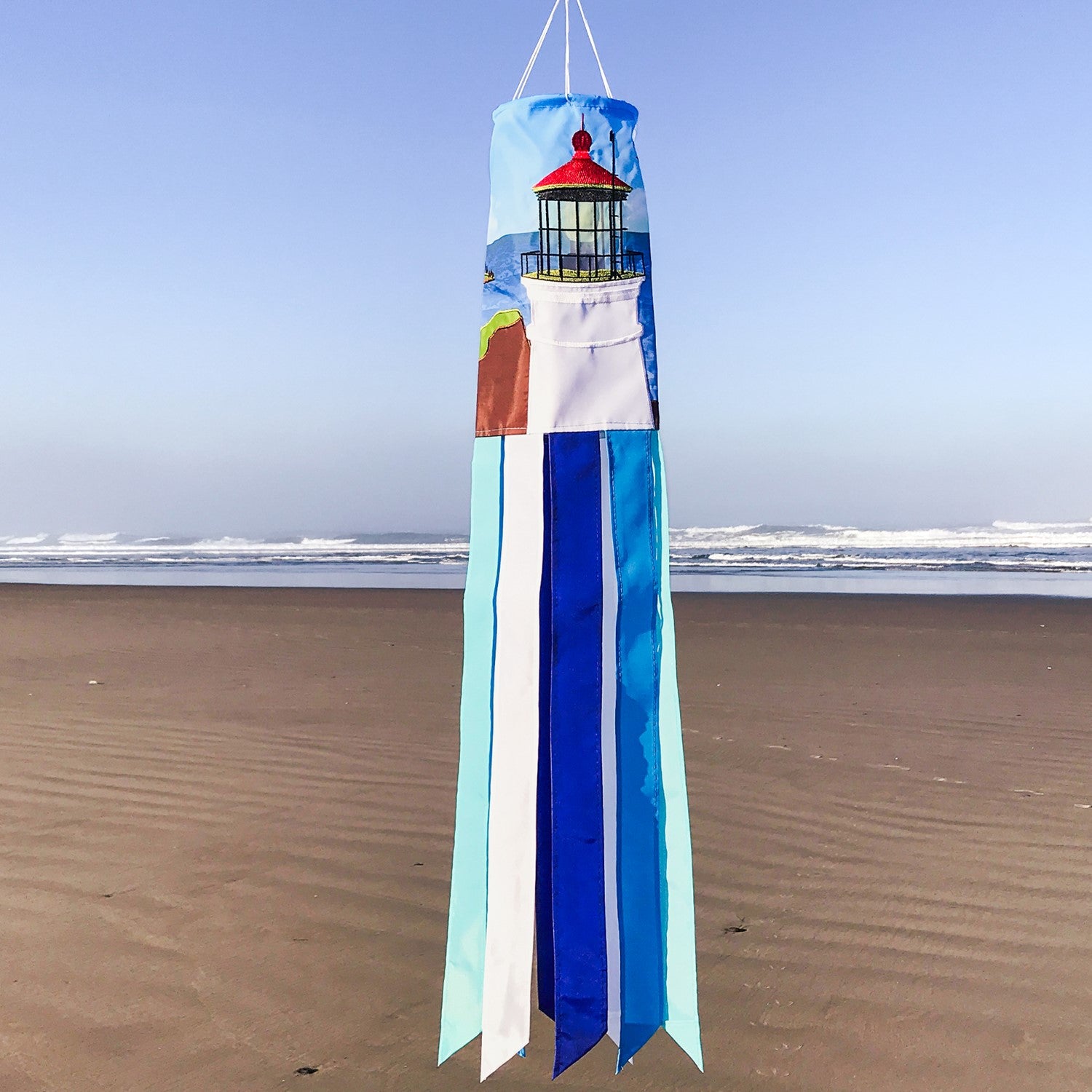 Coastal Lighthouse 40-inch windsock with vibrant lighthouse design and tails hanging elegantly from a garden in a coastal setting.