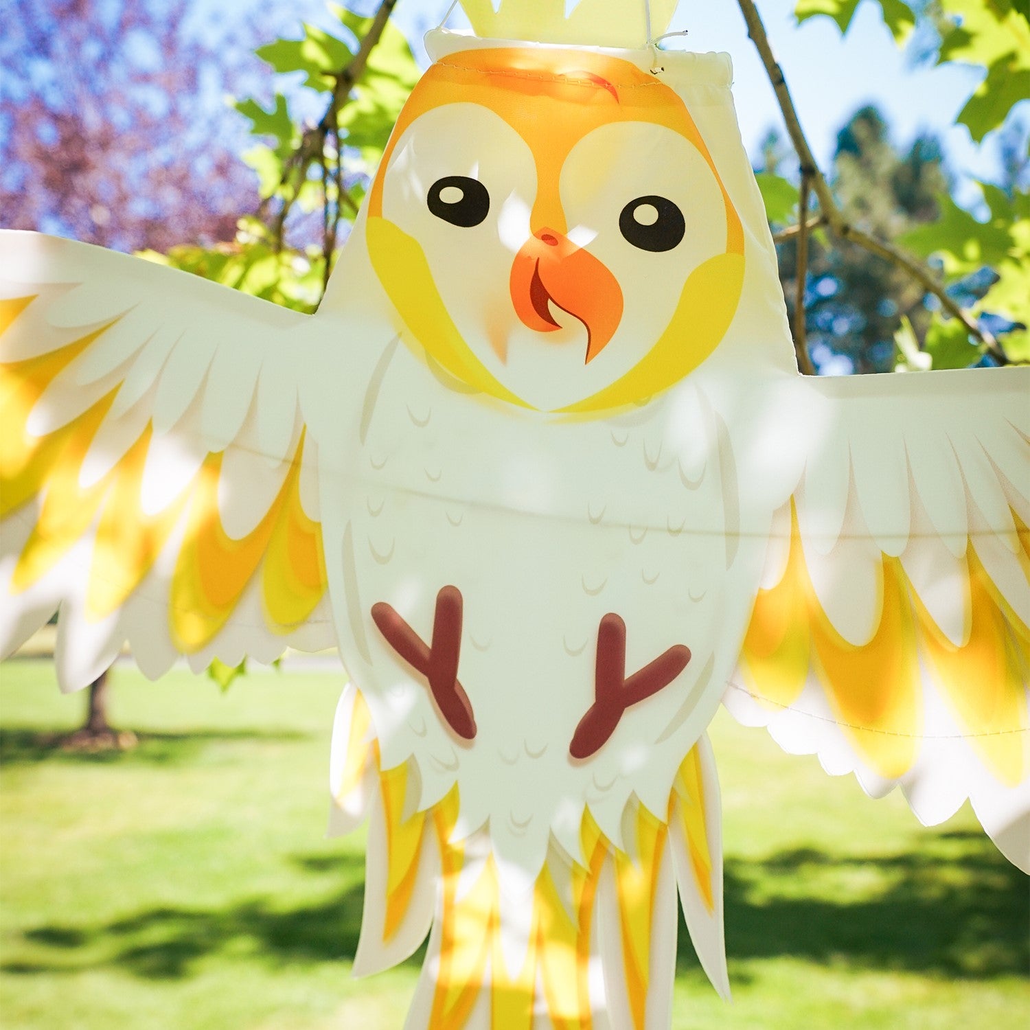 Colorful Cockatoo Windsock flapping gently in the breeze, showcasing its vibrant design with fully spread wings in an outdoor garden setting.