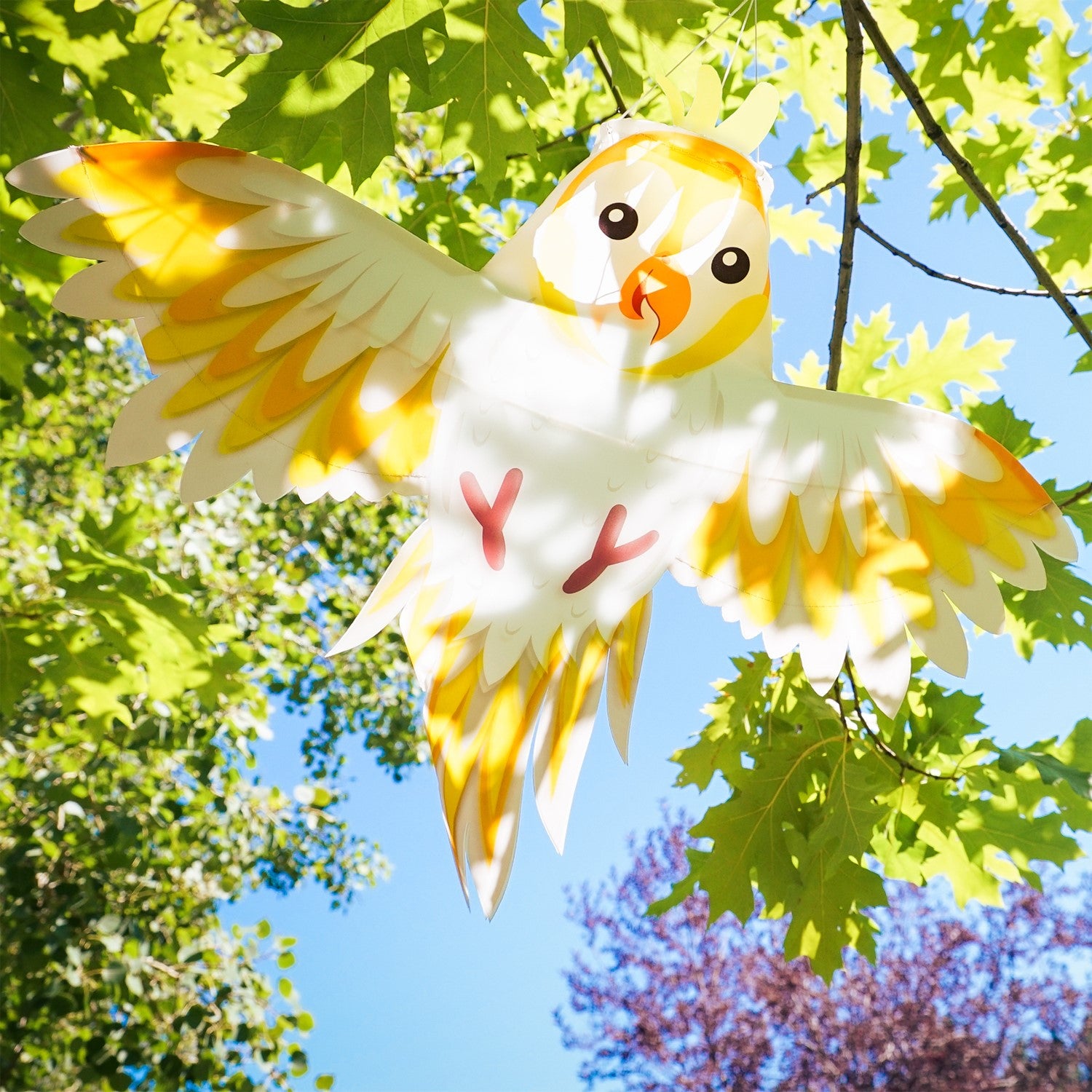 Colorful Cockatoo Windsock flapping gently in the breeze, showcasing its vibrant design with fully spread wings in an outdoor garden setting.