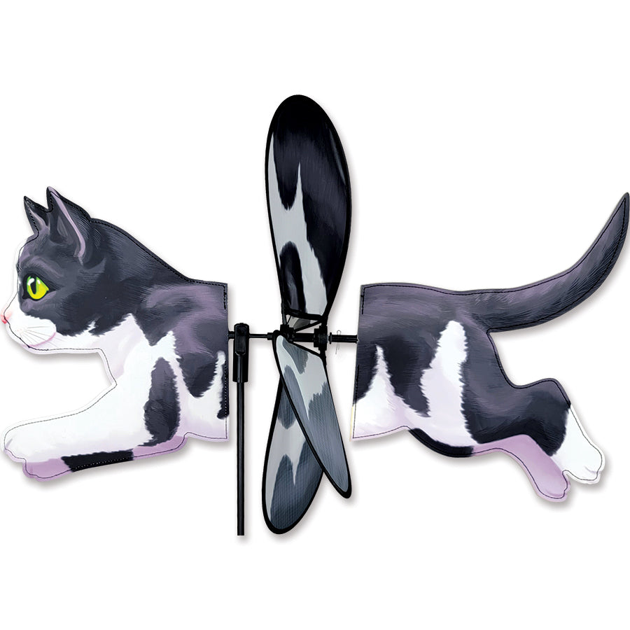 Deluxe Petite Spinner featuring a black and white cat design, spinning in a gentle breeze in a beautifully landscaped garden.