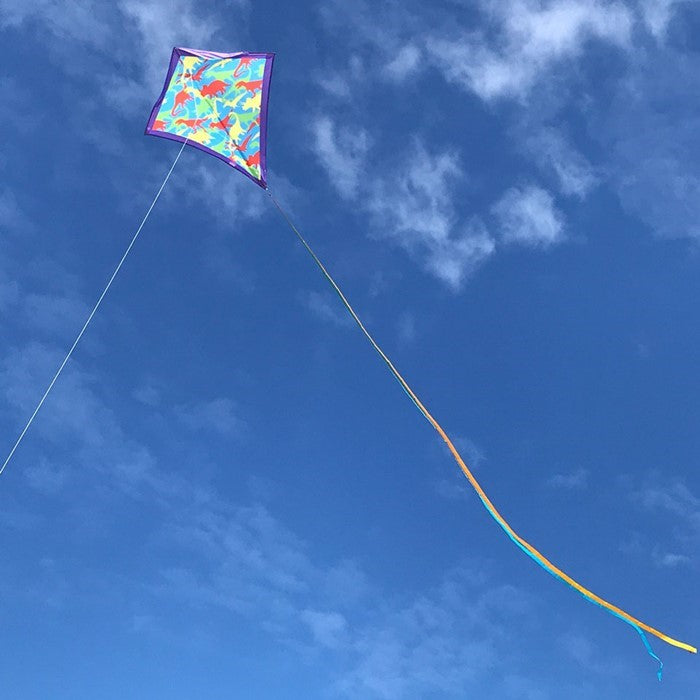 Dinosaur Camouflage 30-inch diamond kite with colorful T-Rex and Pterodactyl designs flying in a clear blue sky during a sunny day.