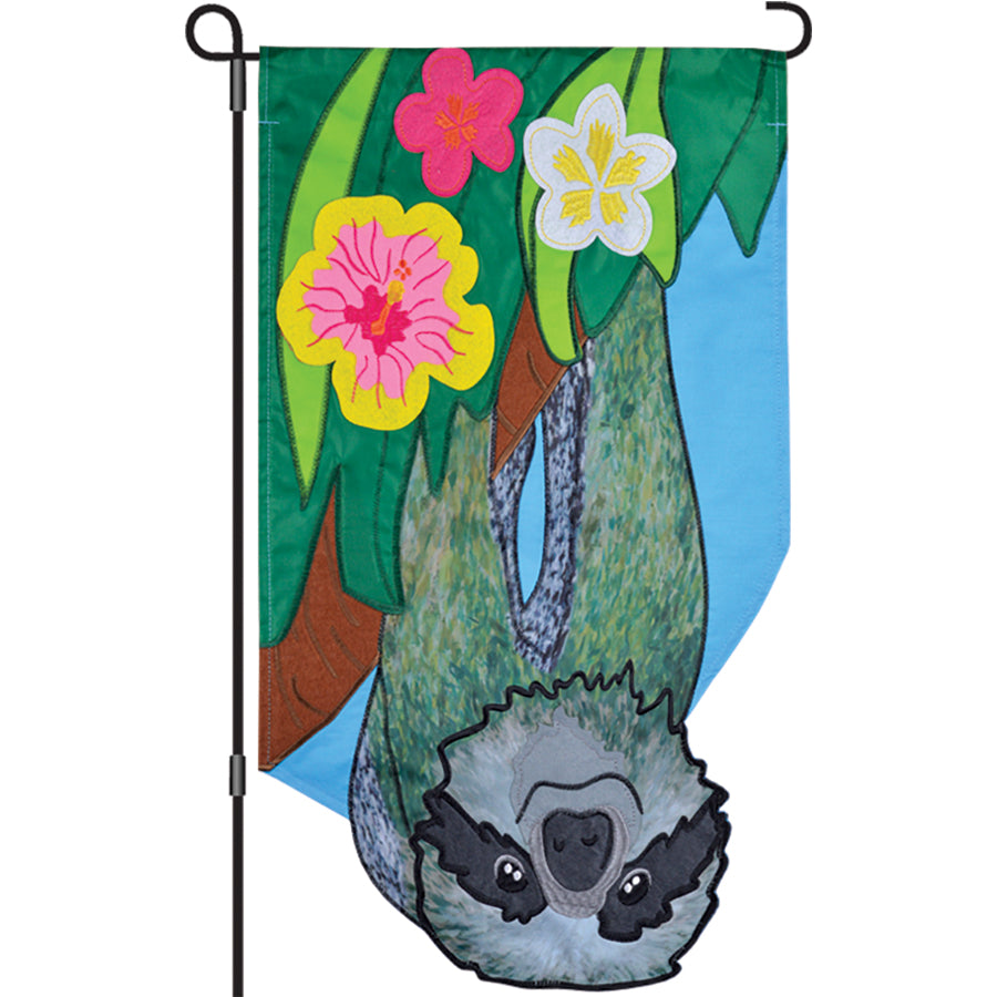 13 in. Enhanced Flag with a colorful sloth design, beautifully embroidered and displayed on a standard garden flag pole in a vibrant garden.
