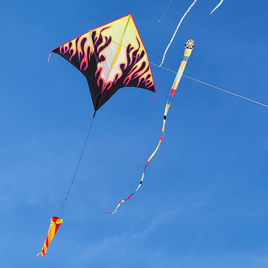 Gyro Delta Kite in Flames flying high against a blue sky with a colorful spinning windsock dancing in the breeze.