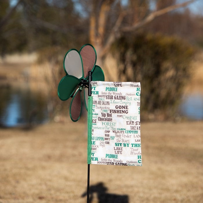 Happy Camper Flower Spinner with colorful camping flag in a garden setting, featuring a vibrant flower design and pivoting pole.