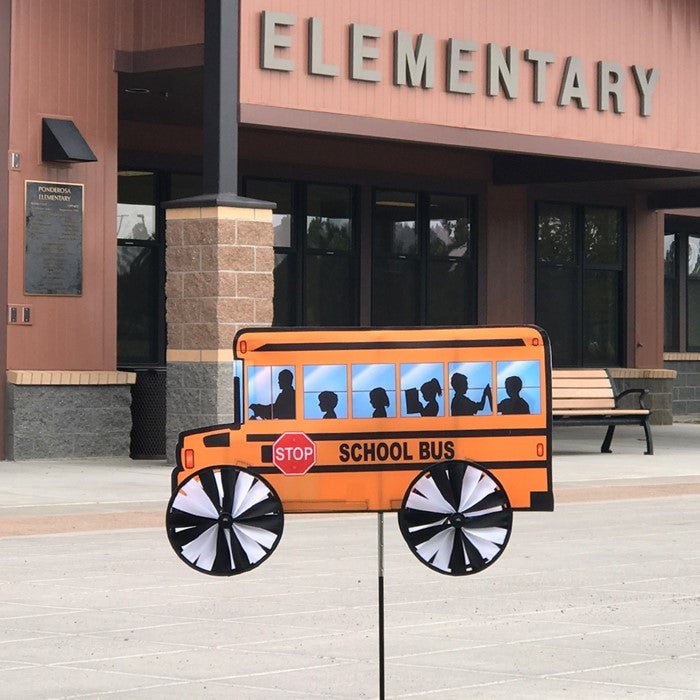 Alt Text: "24-inch school bus spinner with vibrant yellow design and colored wheels, spinning in a garden setting on a bright sunny day.
