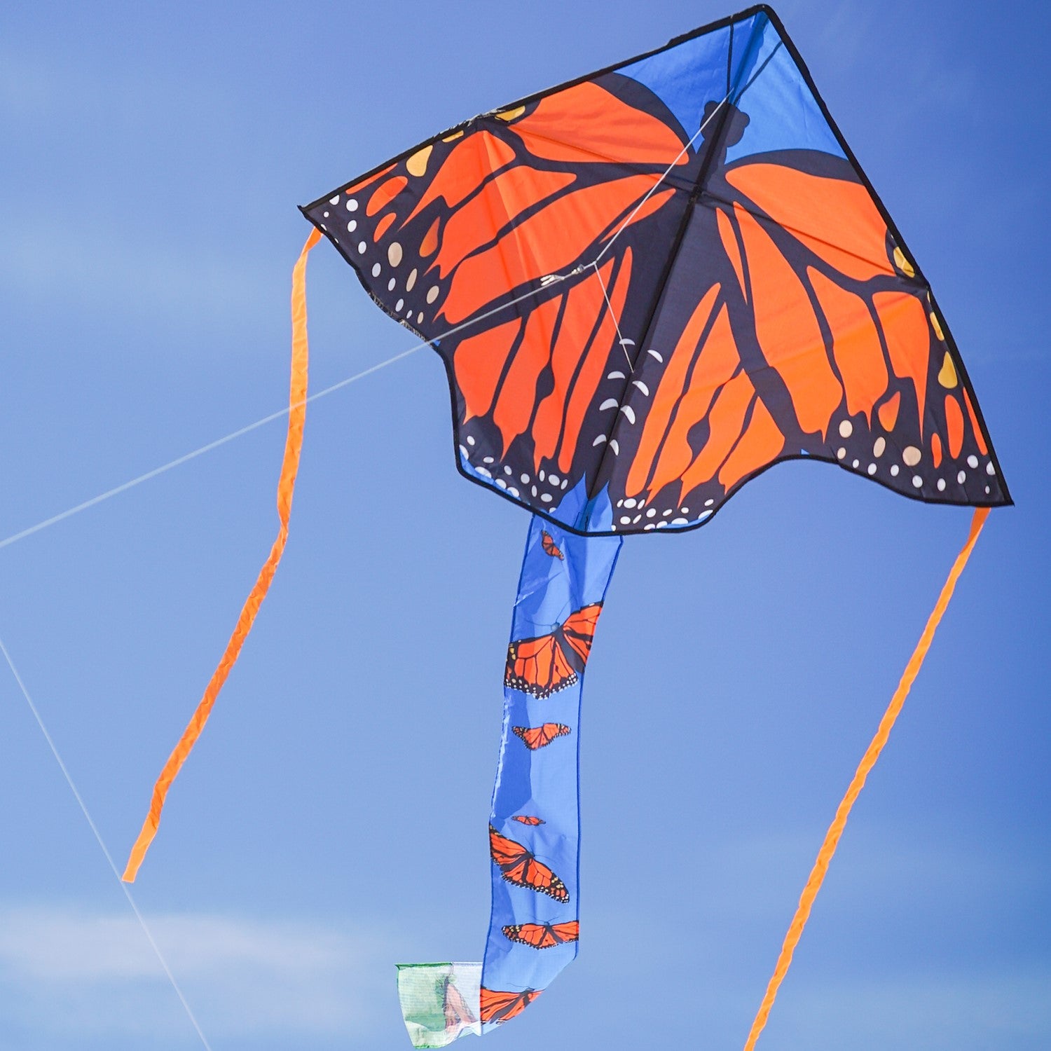 Alt text: "Monarch Swarm 45-inch Fly-Hi Kite soaring through a clear blue sky with colorful butterfly design and streamer tails.