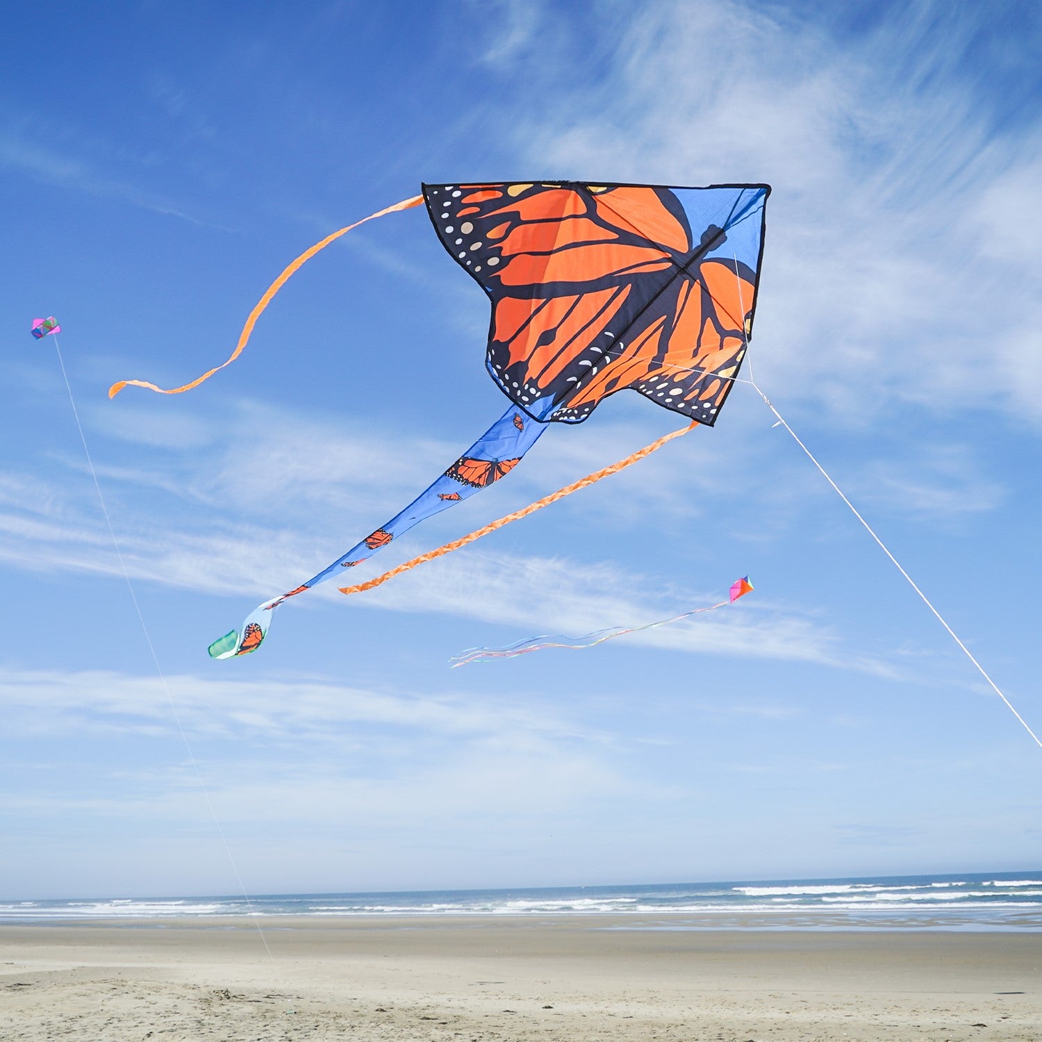 Alt text: "Monarch Swarm 45-inch Fly-Hi Kite soaring through a clear blue sky with colorful butterfly design and streamer tails.