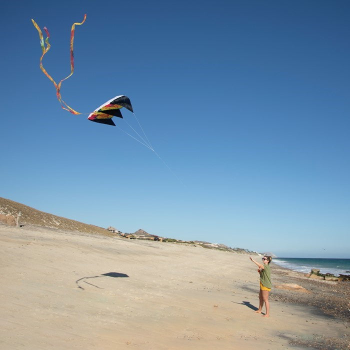 Alt Text: 7.5 Tie Dye Black Air Foil Kite flying against a clear blue sky, showcasing its vivid tie dye pattern and colorful tails in motion.
