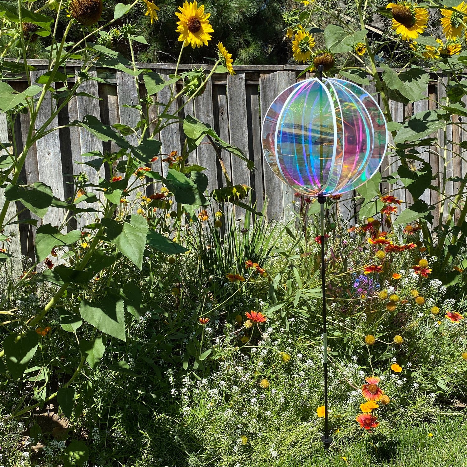 Iridescent 16-inch gazing ball spinner with six shimmering panels reflecting sunlight displayed in a vibrant garden setting.