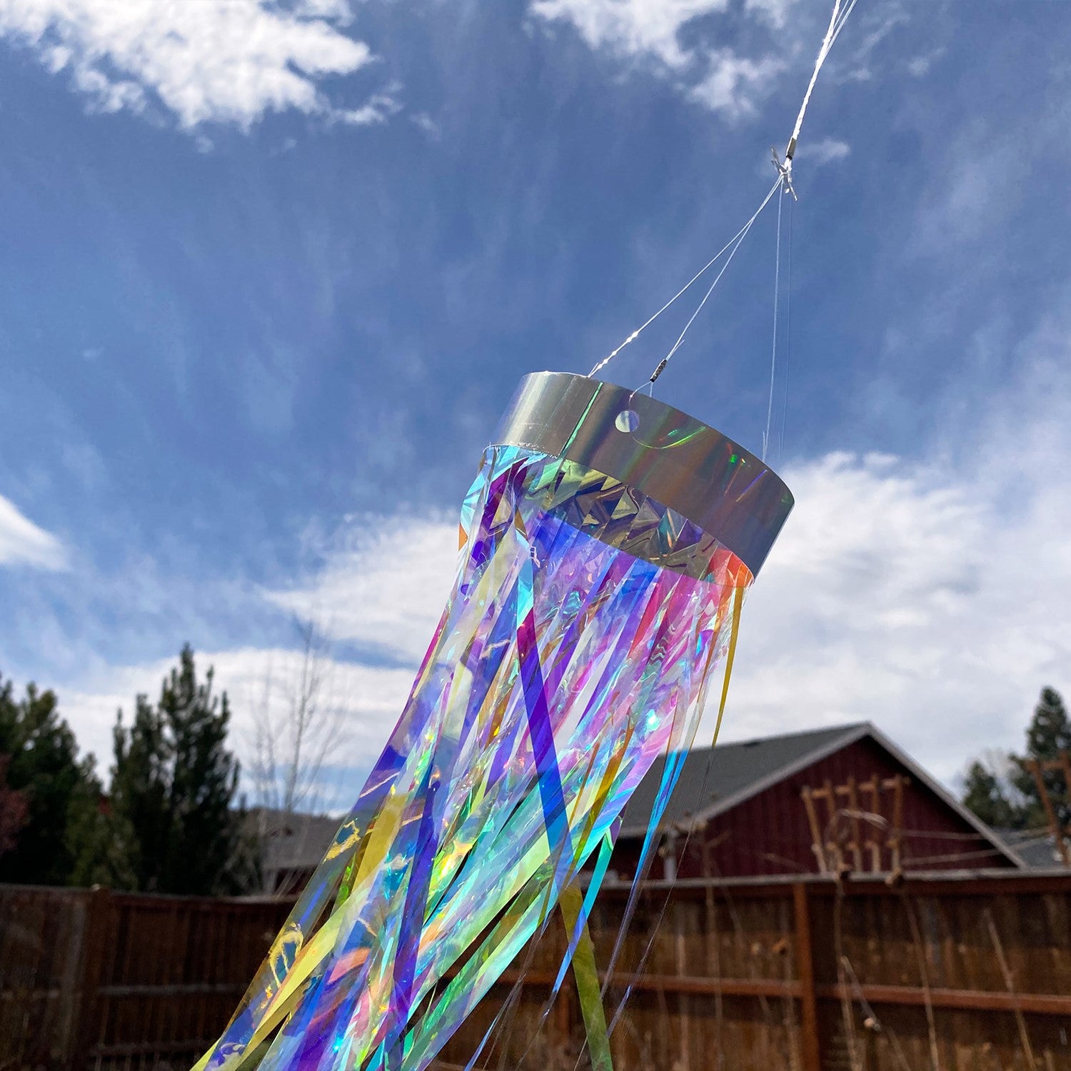 Iridescent 51-inch Mylar windsock with holographic design fluttering in a gentle breeze, creating a colorful display in a garden setting.