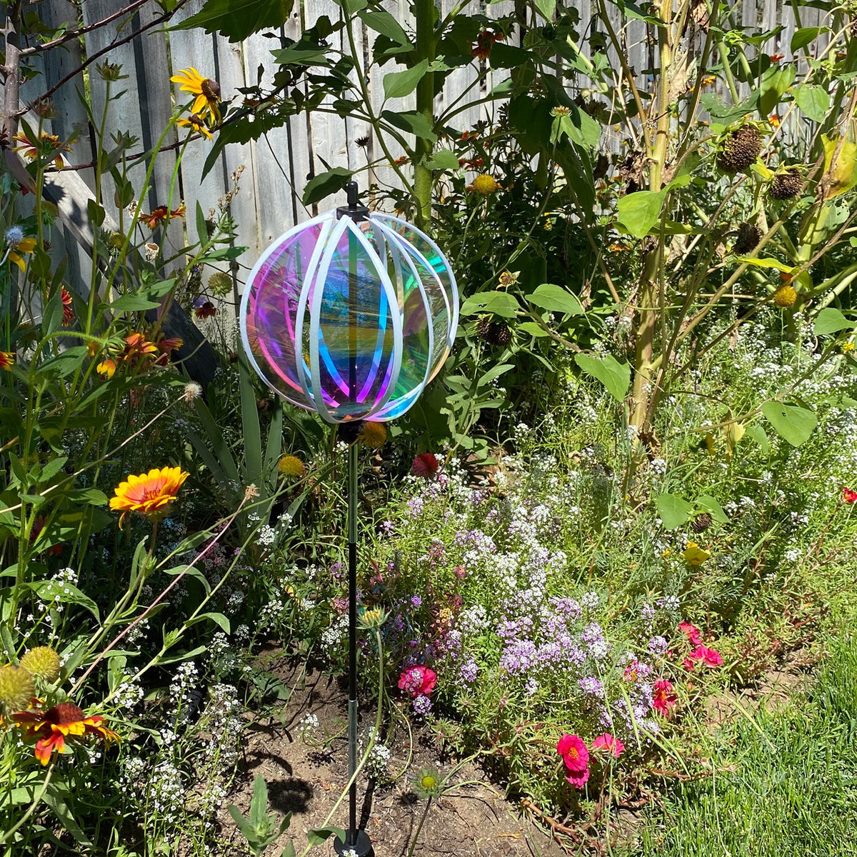 Iridescent 8.5-inch Gazing Ball Spinner reflecting sunlight, showcasing its vibrant colors in a beautifully landscaped garden.