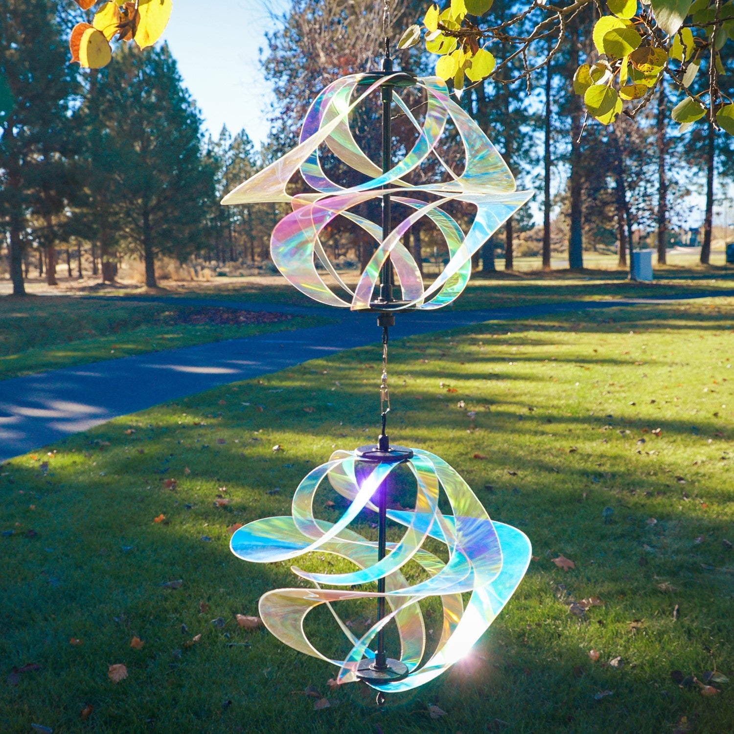 Iridescent Vortex Double Spinner showcasing interconnected Mylar spirals spinning in a sunny garden setting, creating a vibrant visual display.