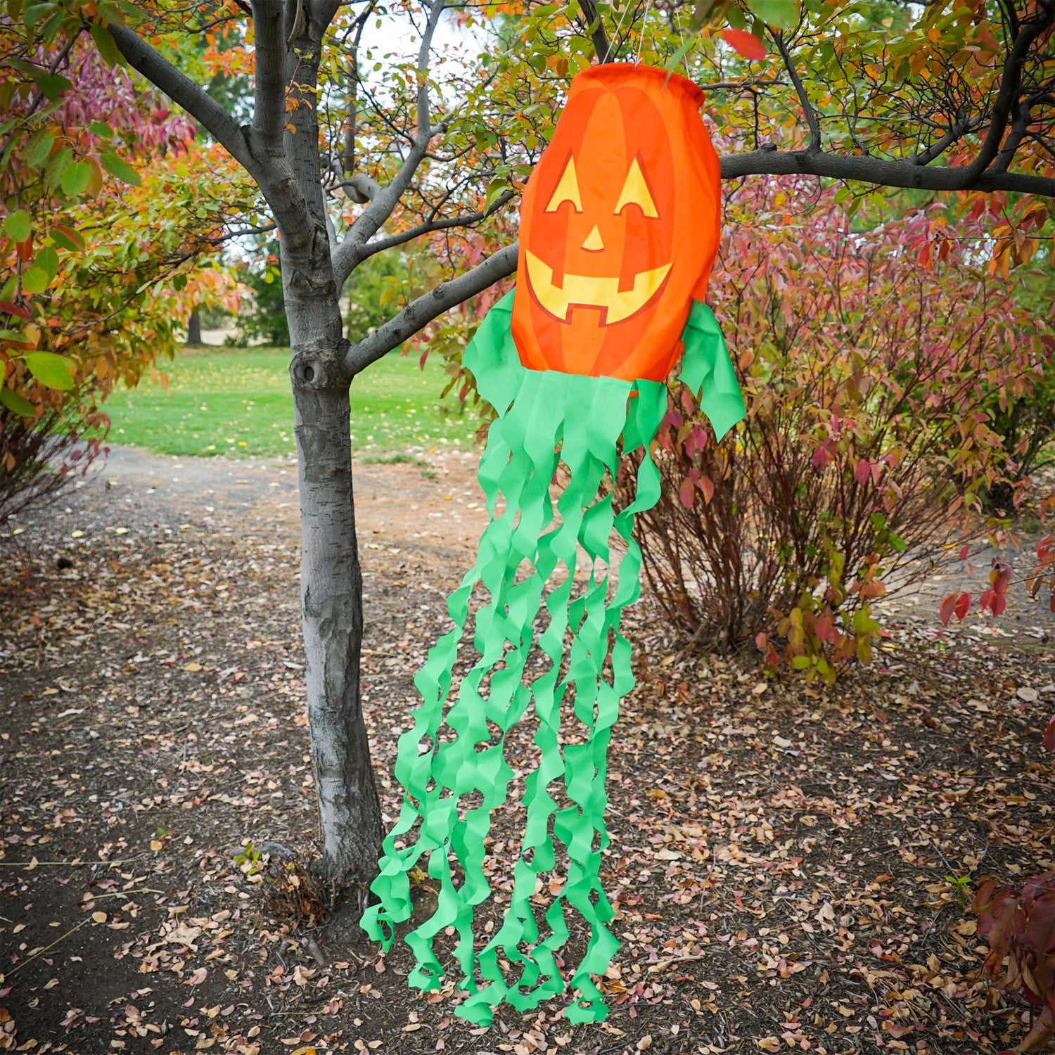 Jack O' Lantern 3D windsock featuring a vibrant pumpkin design and curlie streamer tails, displayed outdoors, fluttering in the breeze.