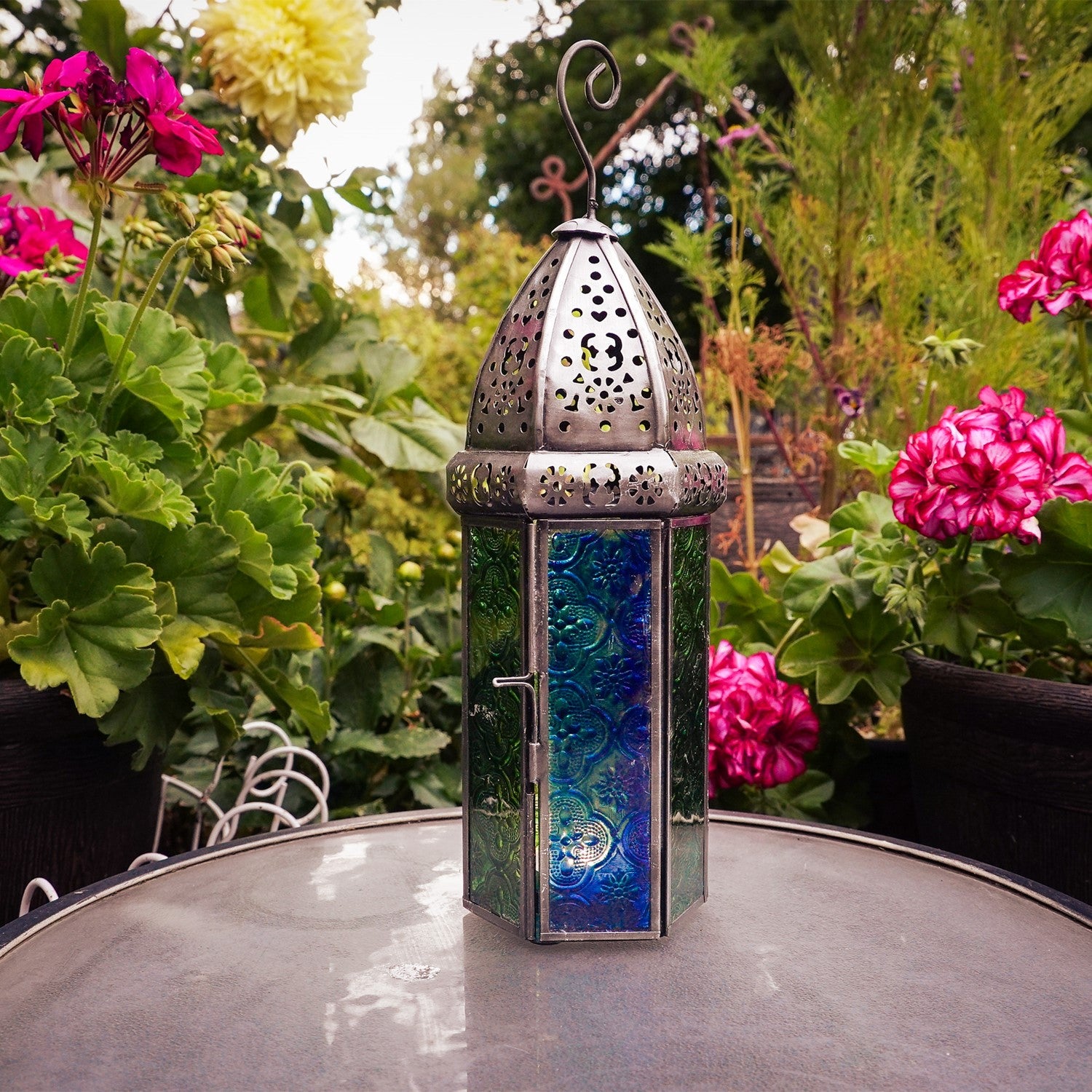 Large Blue & Green Hex Glass Tealight Lantern featuring stamped glass panels and metal frame, hanging gracefully in an outdoor setting.