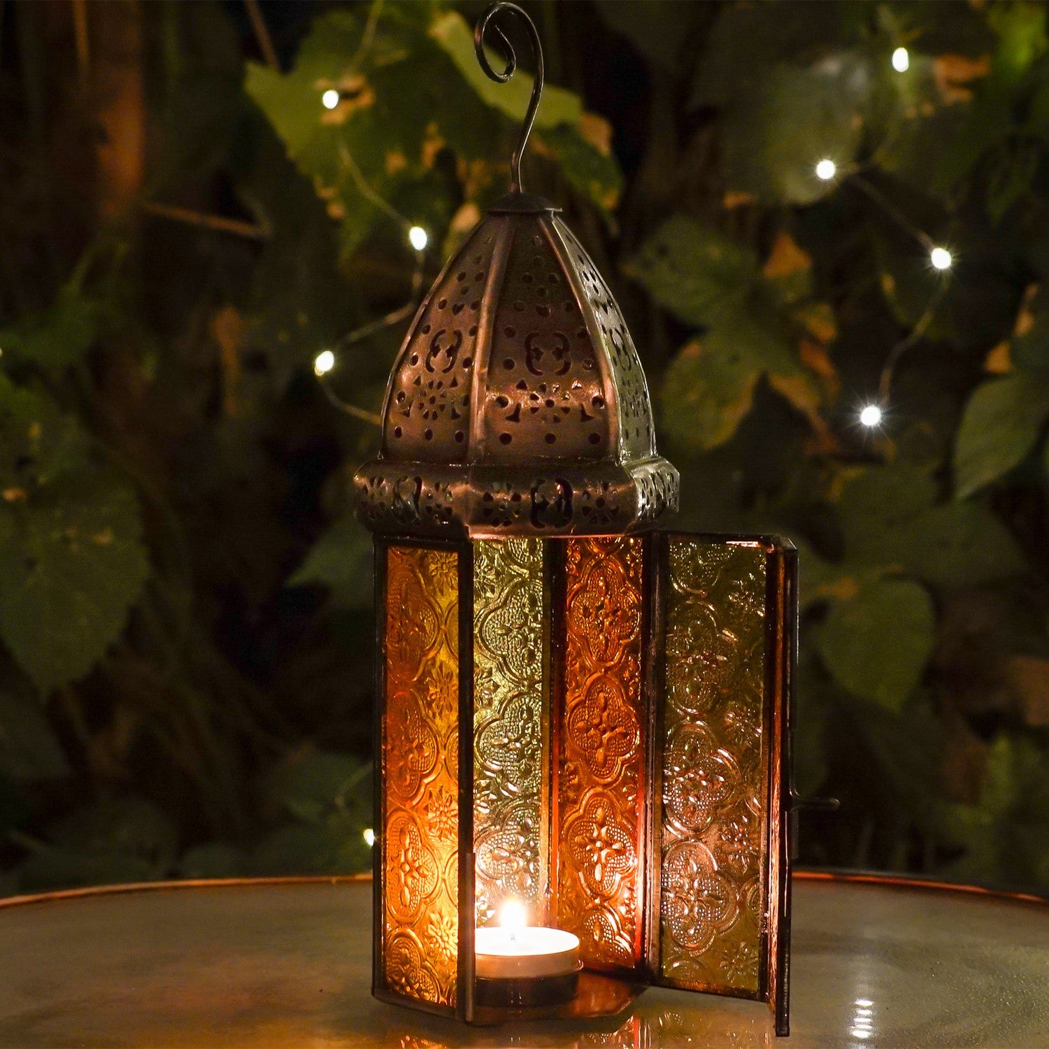 Large Orange & Yellow Hex Glass Tealight Lantern with stamped glass panels and metal accents hanging in an outdoor garden setting.