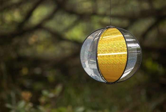 Laser Gold Spinning Globe features six glittering poly panels, designed to spin gently in the wind, displayed in a vibrant outdoor garden setting.