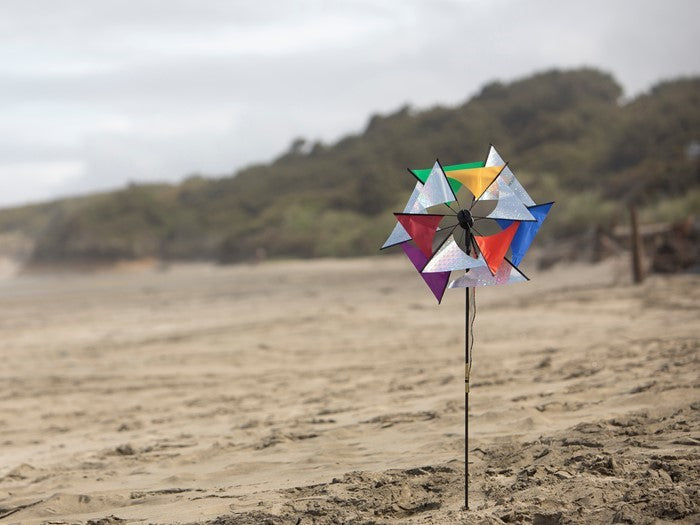 Laser Rainbow Glasshouse Wind Spinner featuring colorful two-wheeled design displayed standing in a garden with blue sky backdrop.