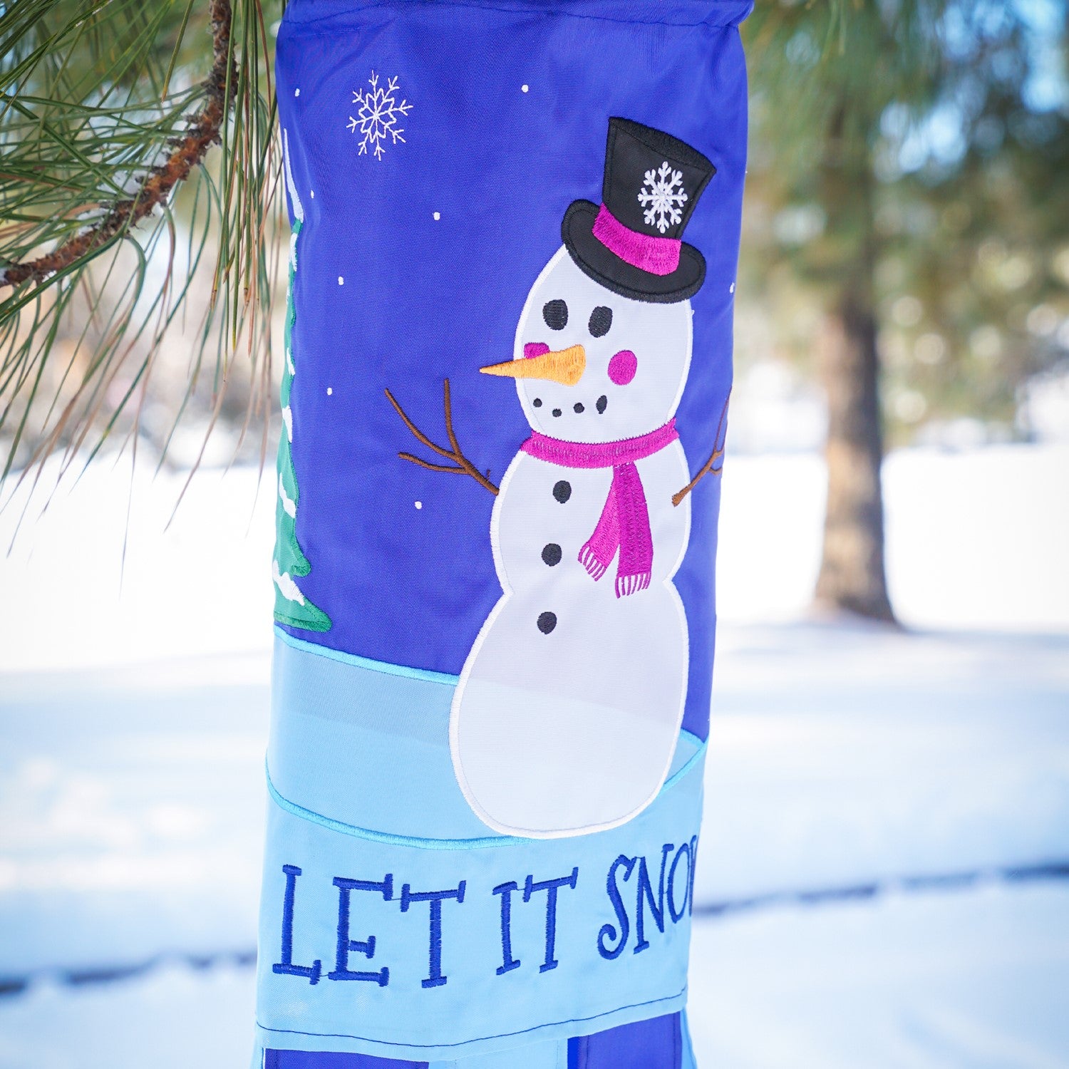 Let It Snow windsock featuring a cheerful snowman design with fluttering tails, perfect for festive winter outdoor decor that adds seasonal charm.