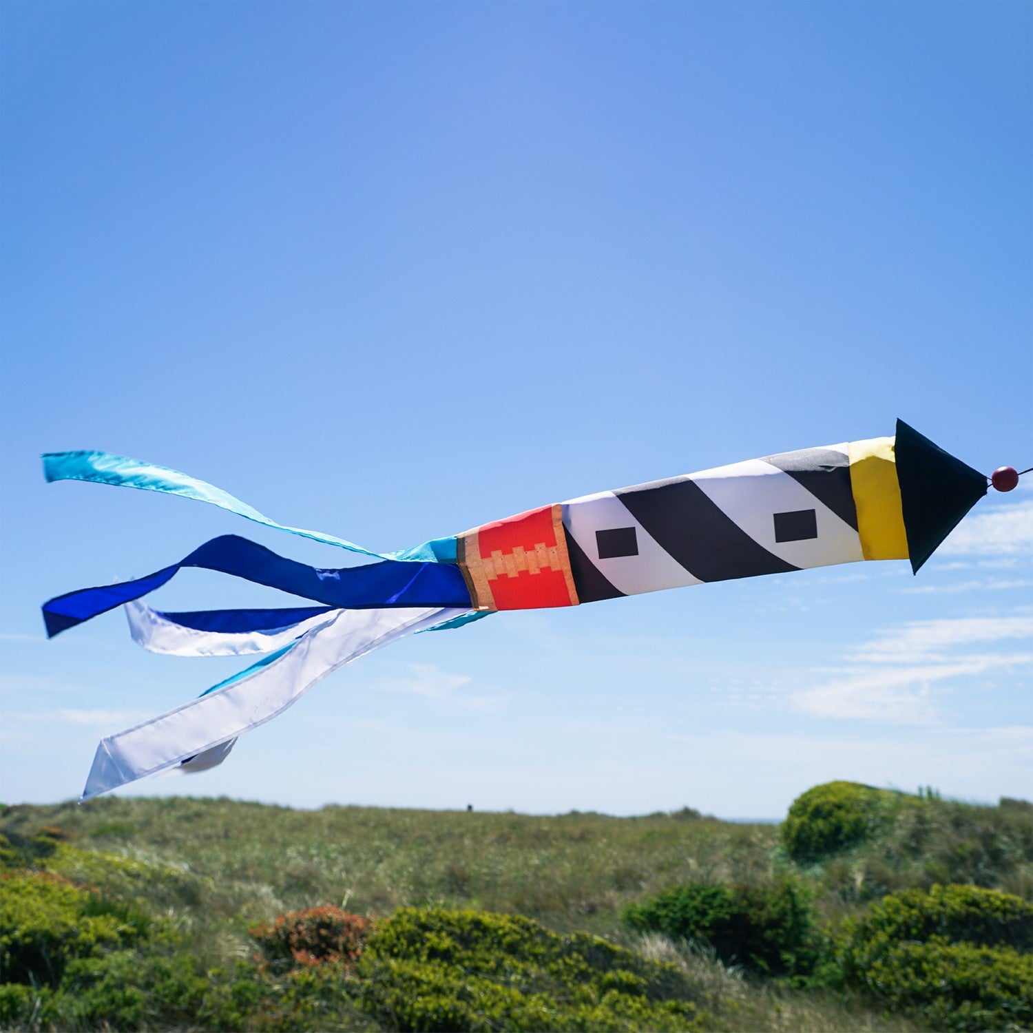 Lighthouse 3D Windsock featuring a colorful lighthouse design with fluttering tails, hanging outdoors in a breezy garden setting.