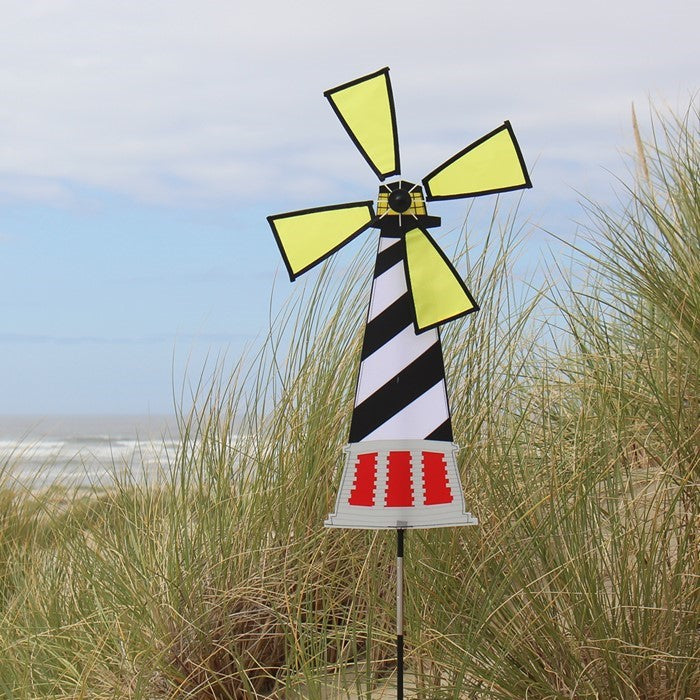 Lighthouse Spinner featuring Hatteras Lighthouse design, displayed outdoors with a colorful, rotating four-panel wheel in a garden setting.