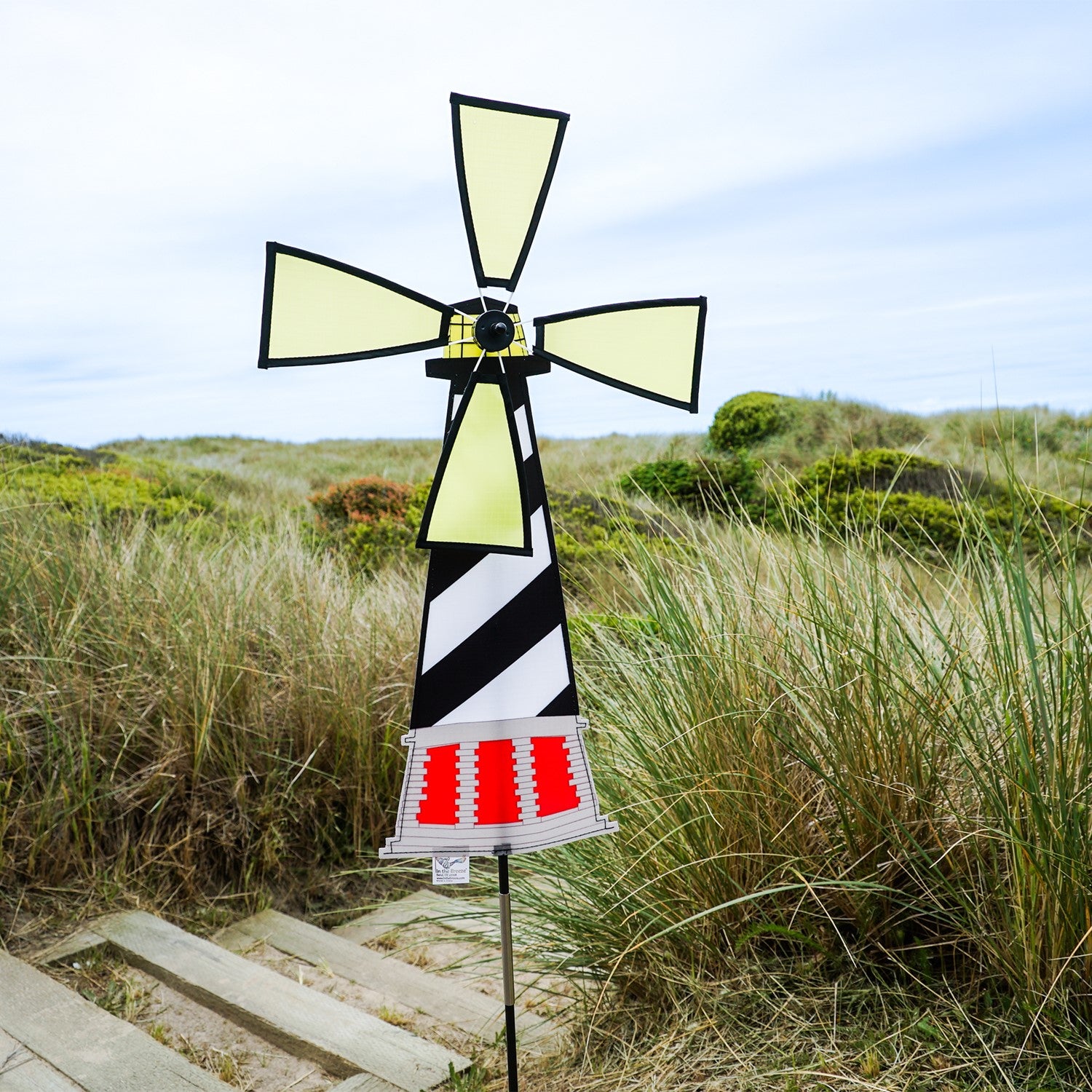 Lighthouse Spinner featuring Hatteras Lighthouse design, displayed outdoors with a colorful, rotating four-panel wheel in a garden setting.