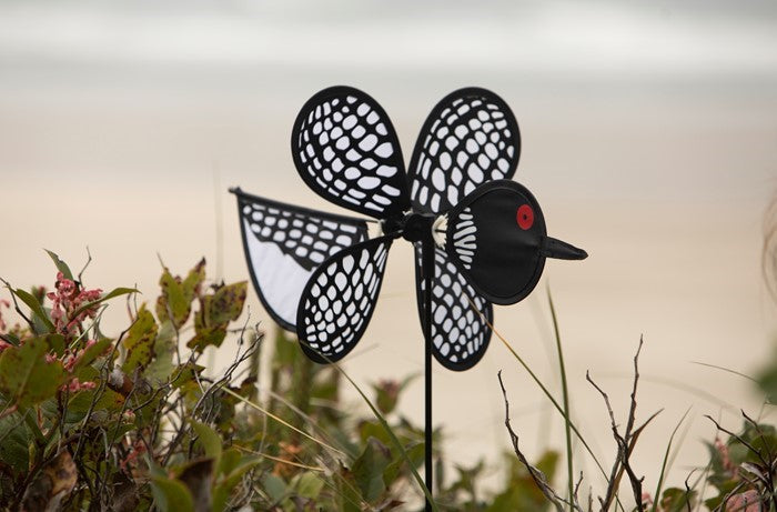 Loon Baby Spinner with colorful baby loons on a 12-inch wheel, spinning gracefully on a 17-inch fiberglass pole in an outdoor garden setting.