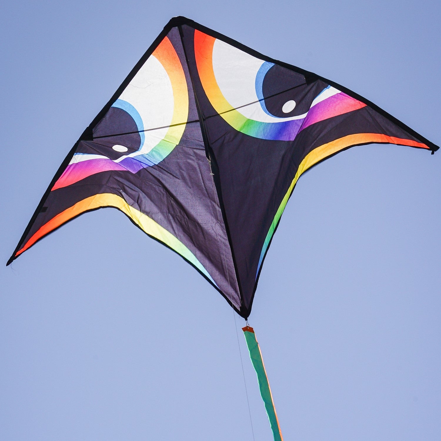 Manu Aurora 72 inch Delta Kite with vibrant colors and a streamer tail flying in a clear blue sky during a sunny day.
