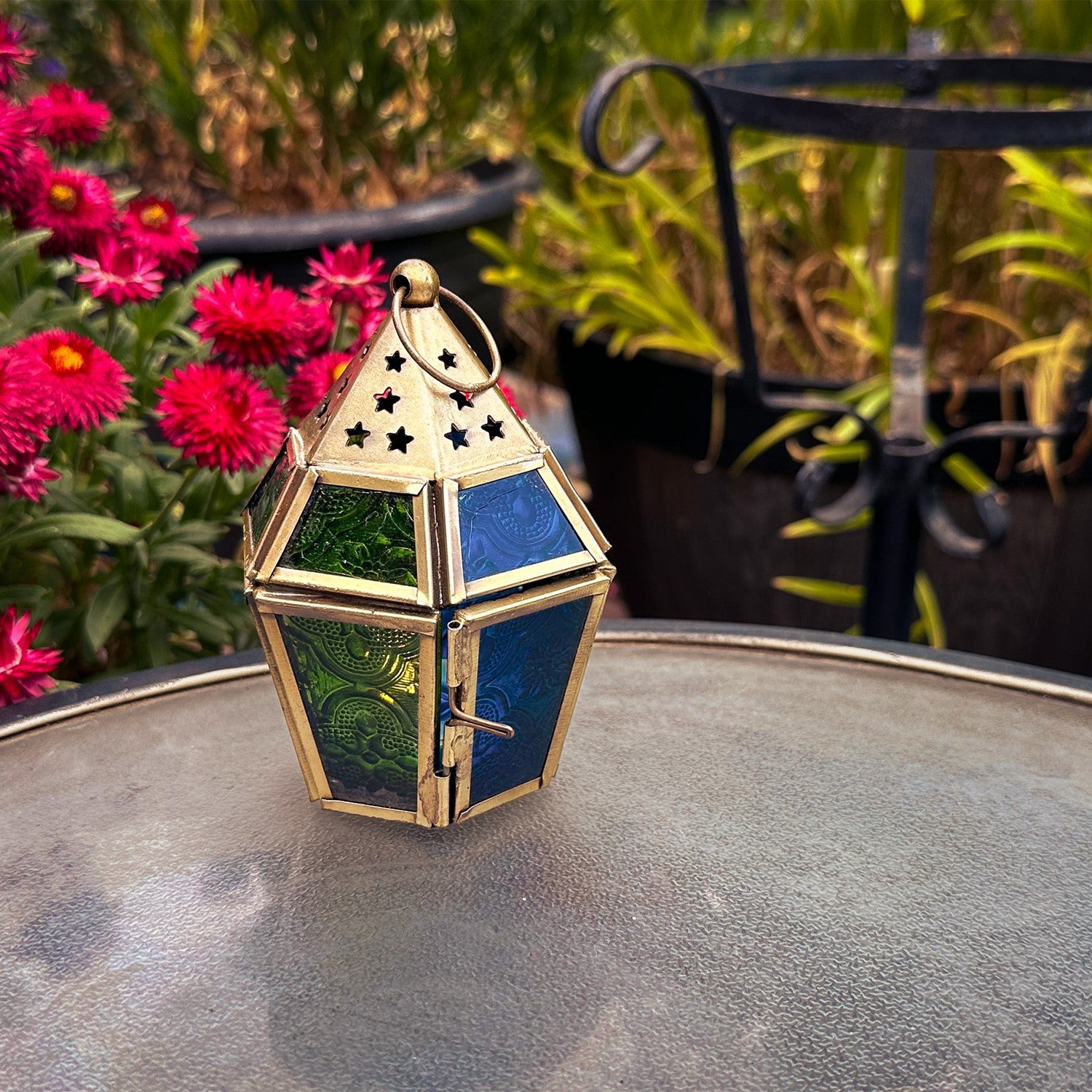 Mini Blue & Green Hex Glass Tealight Lantern with textured glass and brass accents hanging in an outdoor setting, radiating warm candlelight.