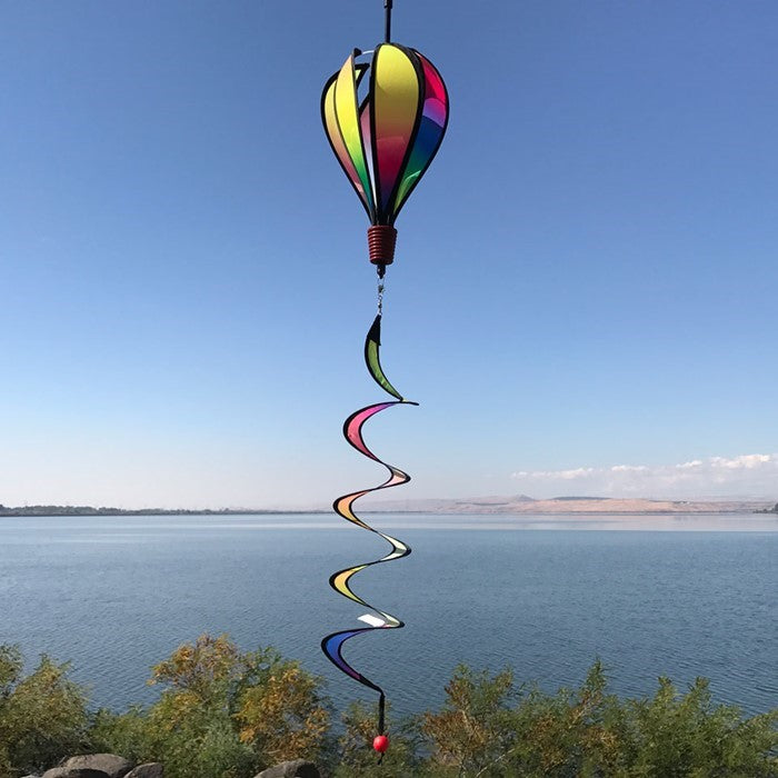 Mini Rainbow Blended Hot Air Balloon spinner with vivid colors floating gently in a garden setting, showcasing its joyful design and curlie tail.