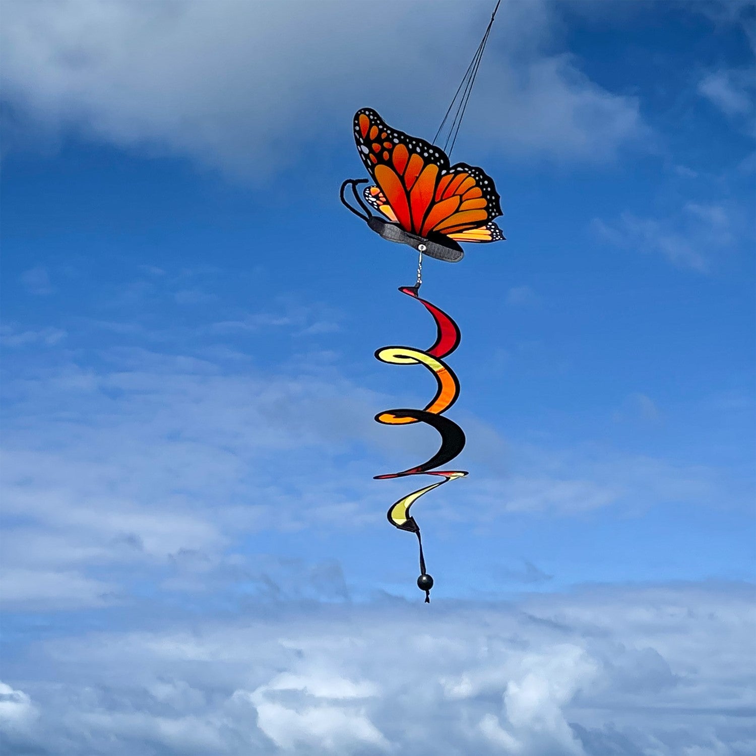Monarch Butterfly Theme Twister featuring moveable wings and a curlie tail, hanging gracefully in a vibrant outdoor garden setting.