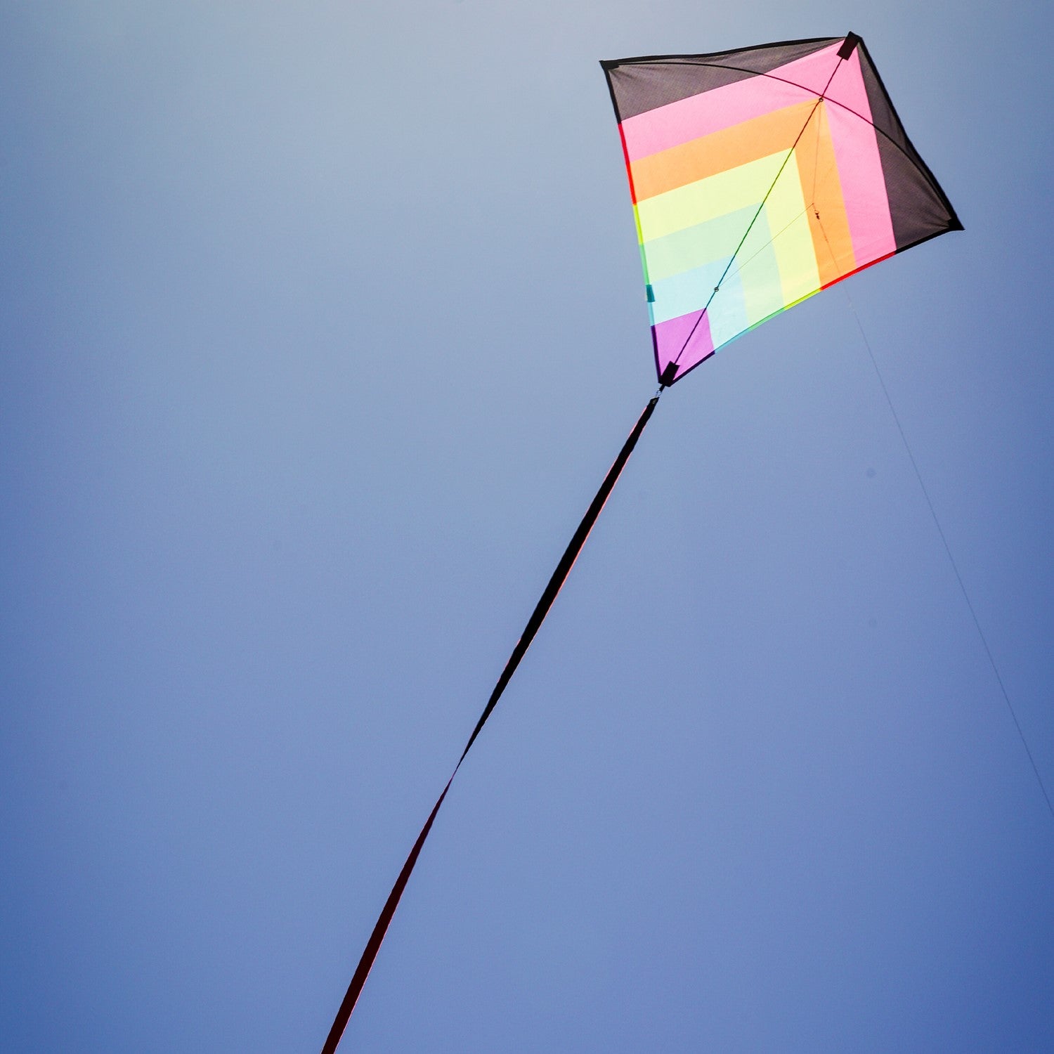 Neon Fiesta 30' Diamond Kite flying in a clear blue sky, featuring bright colors and long flowing tails, showcasing its stunning design.