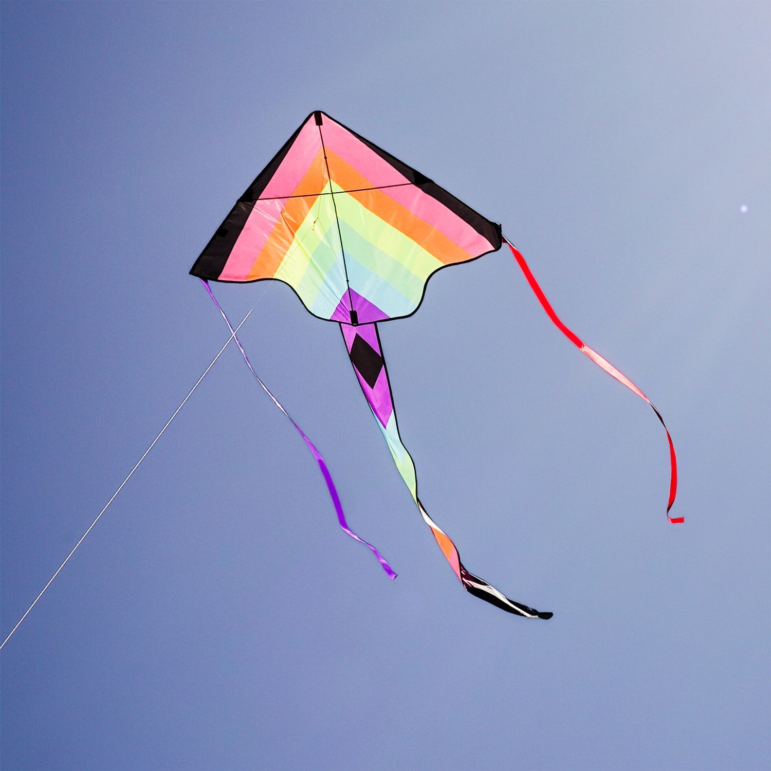 Neon Fiesta 46-inch Fly-Hi Kite soaring high in a blue sky, featuring a vibrant printed design and streamer tails, ideal for family enjoyment.