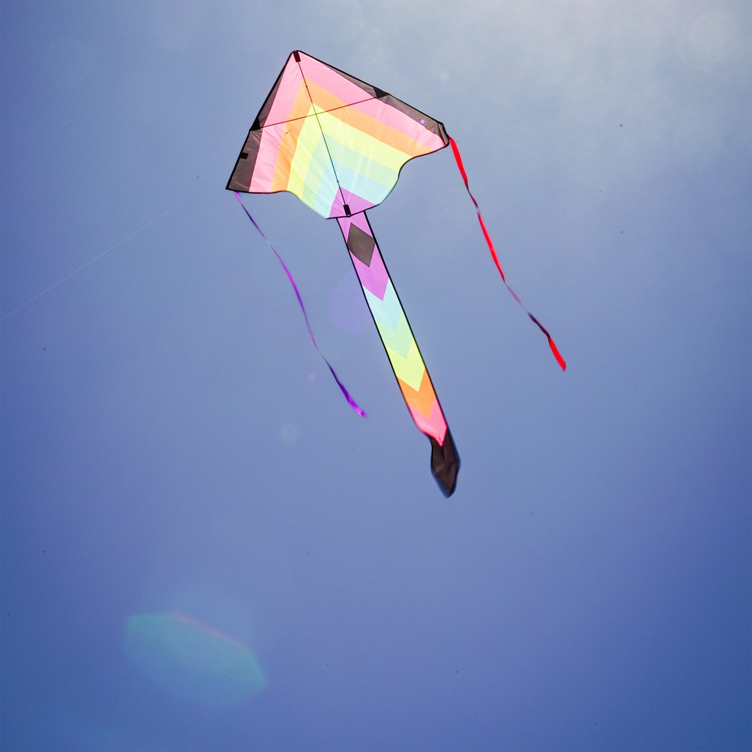 Neon Fiesta 46-inch Fly-Hi Kite soaring high in a blue sky, featuring a vibrant printed design and streamer tails, ideal for family enjoyment.
