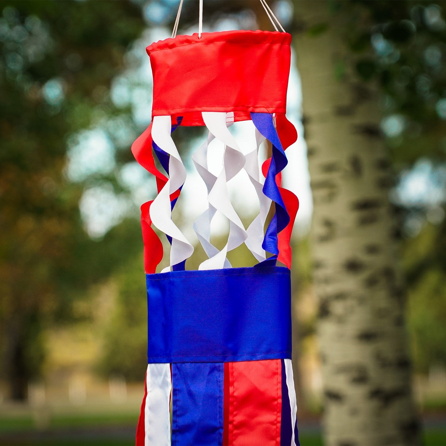 Patriot Twistair windsock featuring red, white, and blue colors with twisted curls, elegantly displayed in a garden setting.