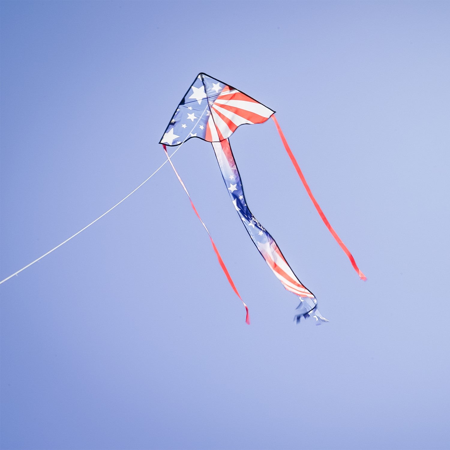 Patriotic 30-inch Mini Fly-Hi kite displaying bright stars and stripes design flying in the sky with attached 60-inch streamer tails.