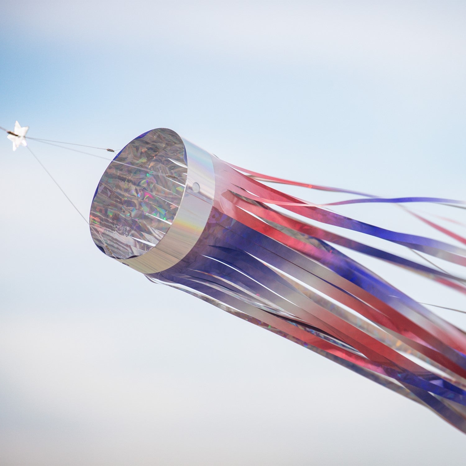 Patriotic 51 inch Mylar windsock in red, white, and blue, shimmering in sunlight while fluttering in the breeze, perfect for festive outdoor decoration.