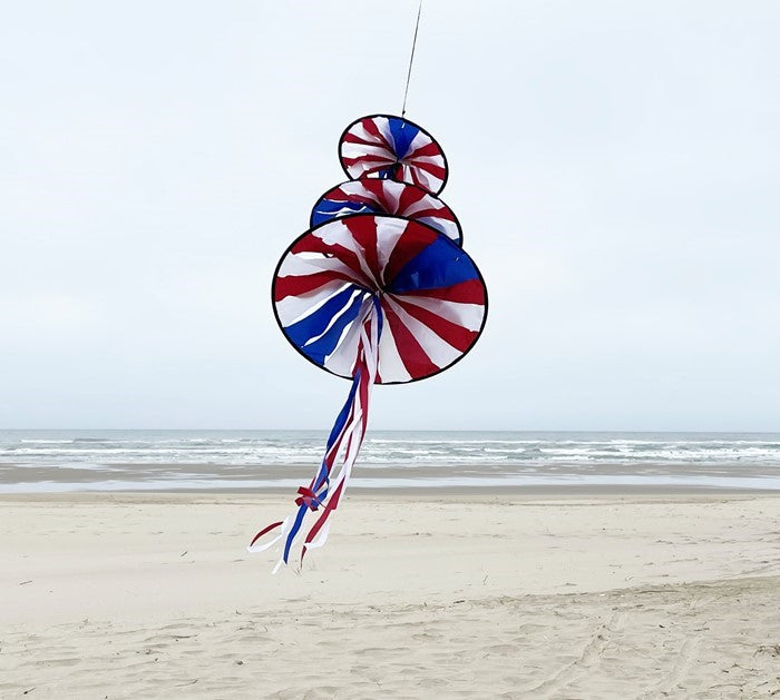 Patriotic Triple Jelly wind decoration featuring three spinning structures in red, white, and blue colors, hanging outdoors in a garden setting.